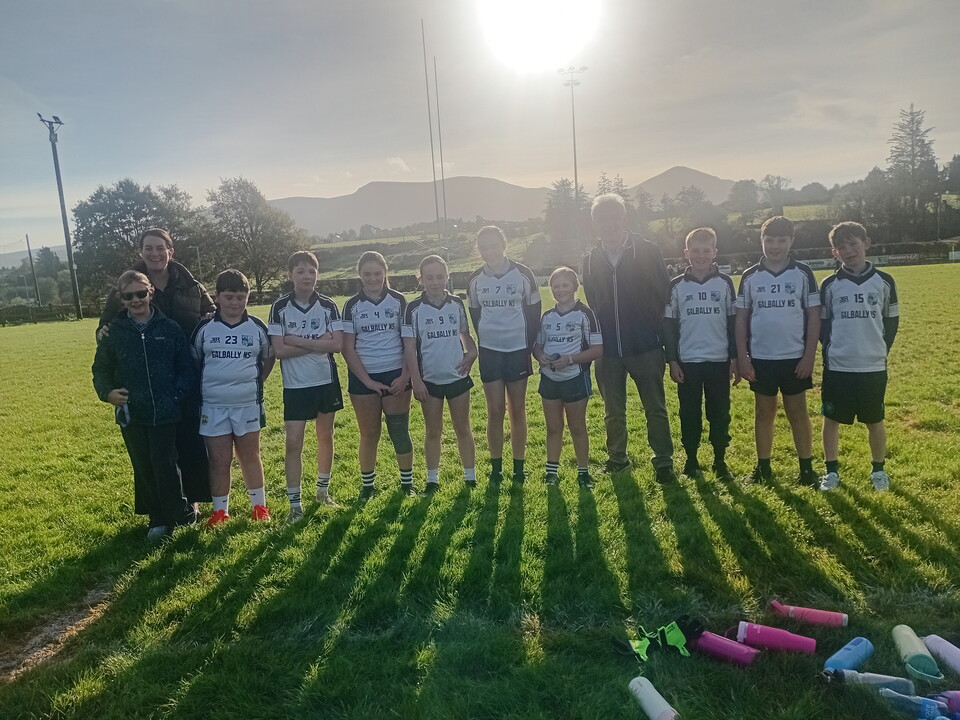 A group of young Gaelic football players on a field with their coaches and equipment.