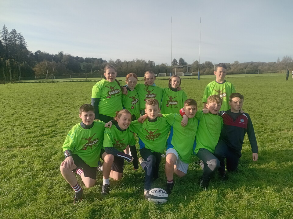 Rugby players in green shirts posing for photo with a rugby ball in front