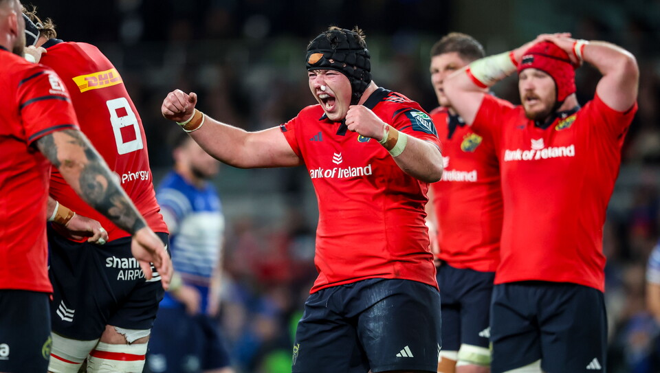 Munster rugby players celebrating a win; two wearing red, two wearing blue
