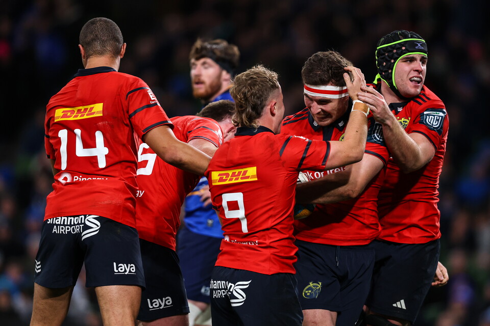 Rugby players in red jerseys celebrate a try with raised arms in a stadium.