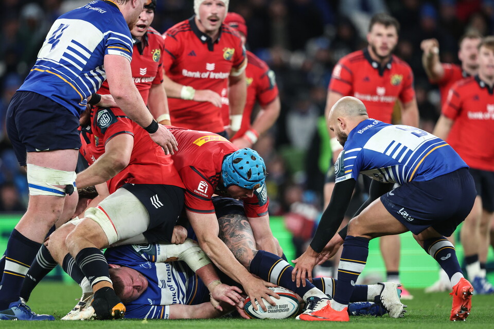 Players in red and blue jerseys compete for the rugby ball on a sports field.