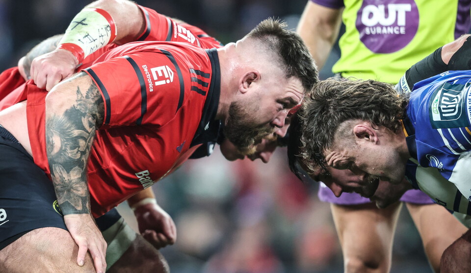 Two rugby players lock heads; one in red, the other in blue, surrounded by teammates.