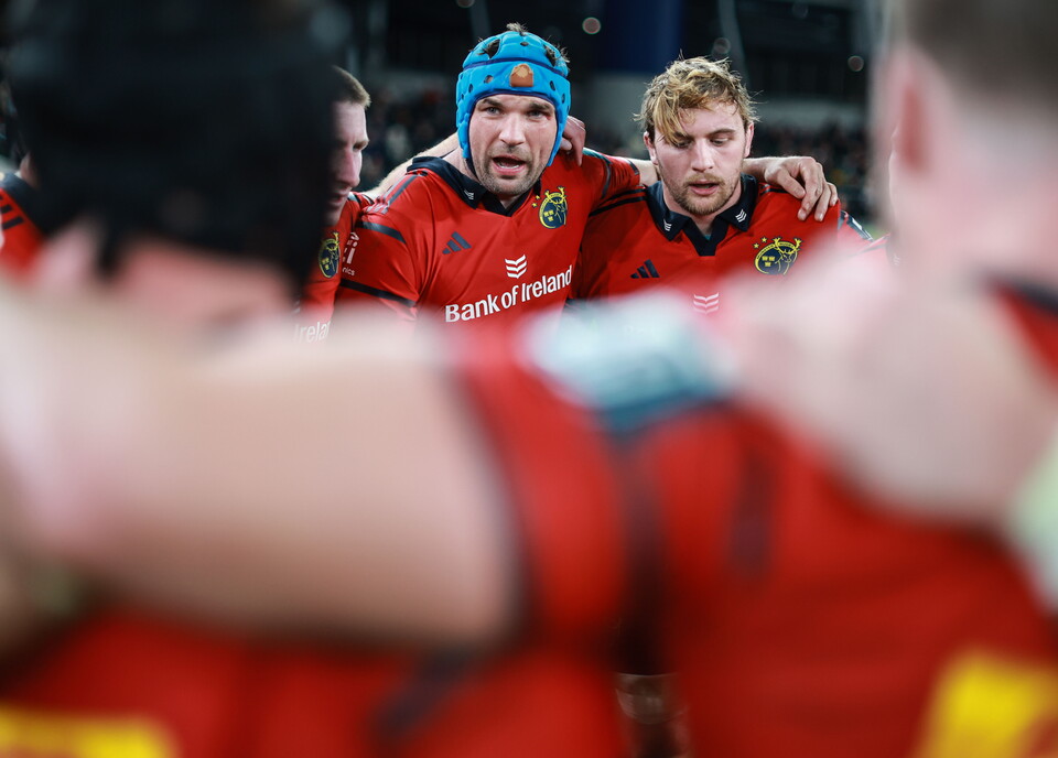 Five players in red rugby shirts huddle together, one wearing a blue hat.