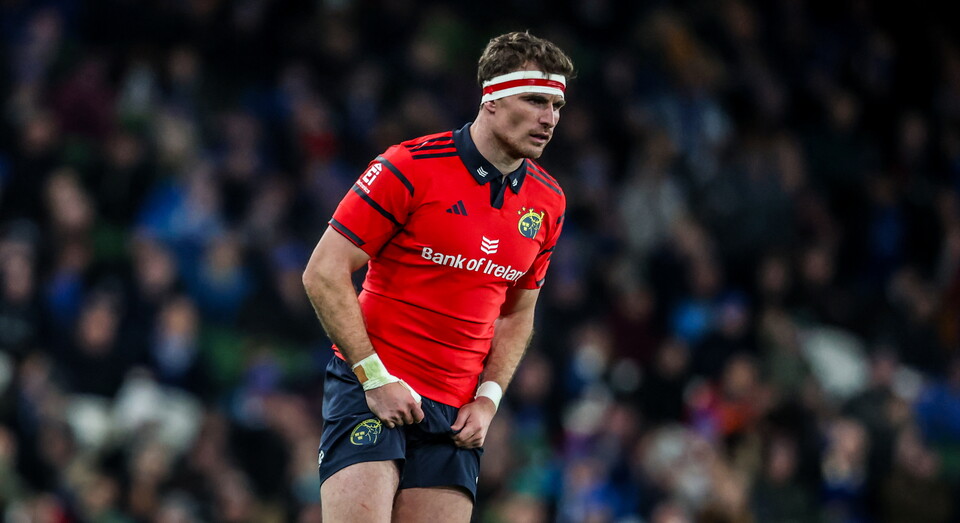 Rugby player in red jersey stands on field with hands on hips