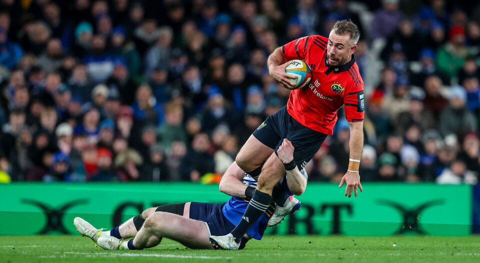 A rugby player in a red jersey runs with the ball during a match.