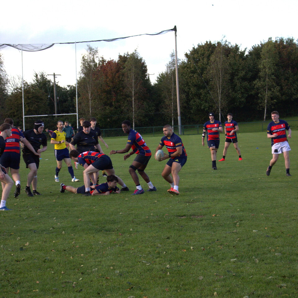 Players in red and black striped shirts and shorts playing rugby on a grass field.