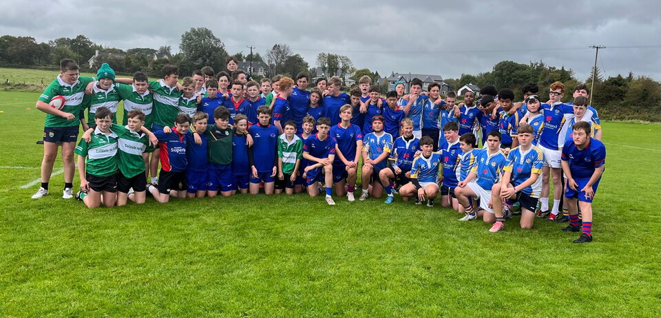 Group of players in blue and green kits posing for a photo on a grassy field.