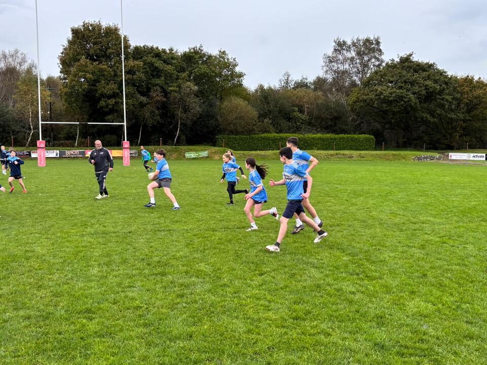 Several people in blue shirts and shorts run across a grass field on a cloudy day.