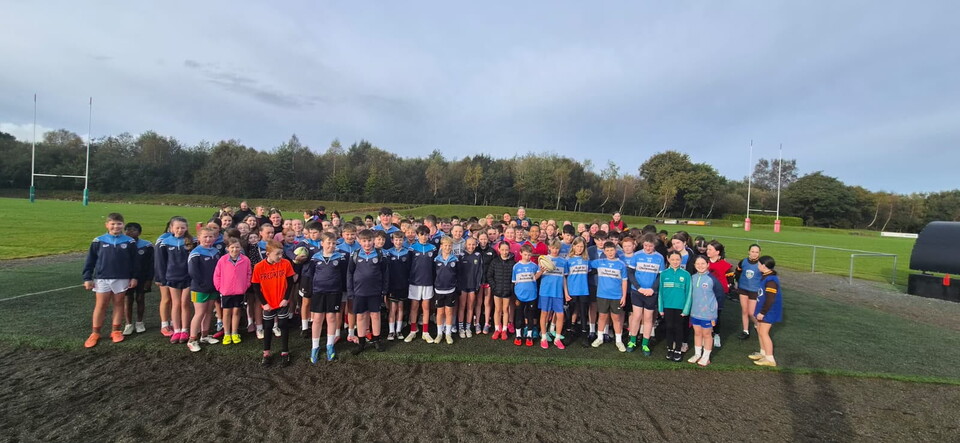 A large group of people wearing blue jerseys and sneakers stand in a circle on a muddy field.