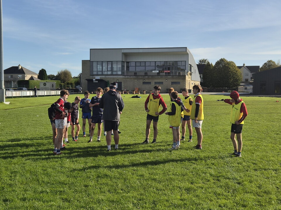 A team of players in yellow and red jerseys discuss strategy on a field.
