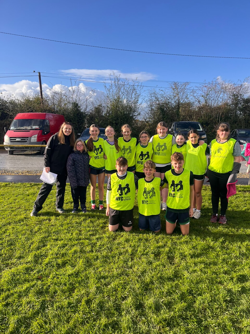 Group of kids and adults in yellow vests posing for a photo on a grassy field.