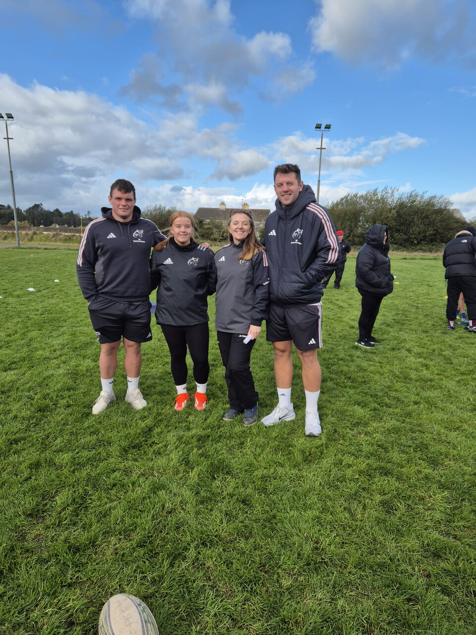 Four people in sportswear standing on a field with a rugby ball in front