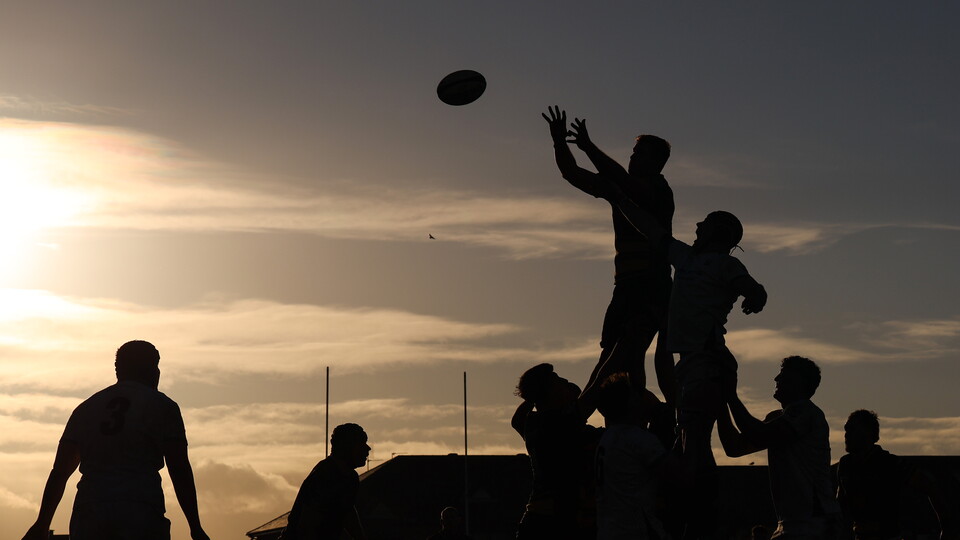 Rugby players in silhouette during a match as the sun sets behind them.