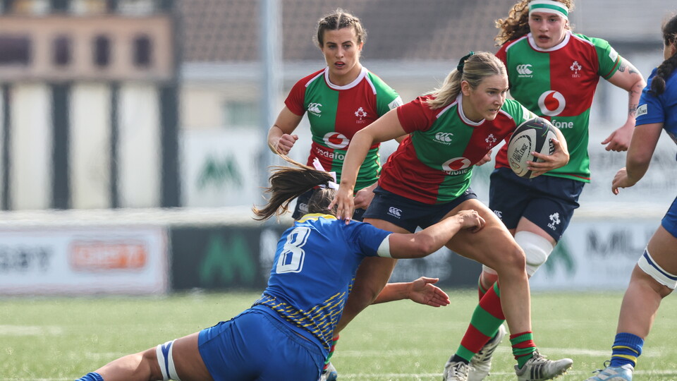 Players in red, green and blue jerseys play rugby on a field.