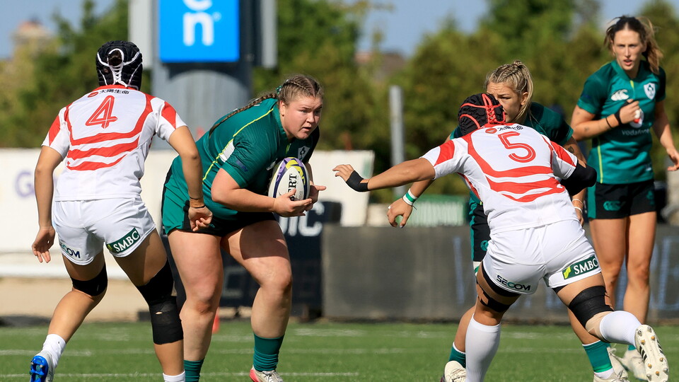 Women rugby players in green and white jerseys on a field, one player holds the ball.