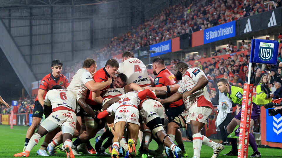 Rugby players in white and red jerseys fight for the ball in a stadium.
