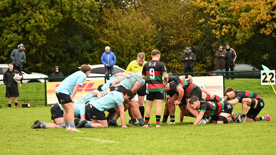 Players in maroon and black stripes scrum against players in blue jerseys.