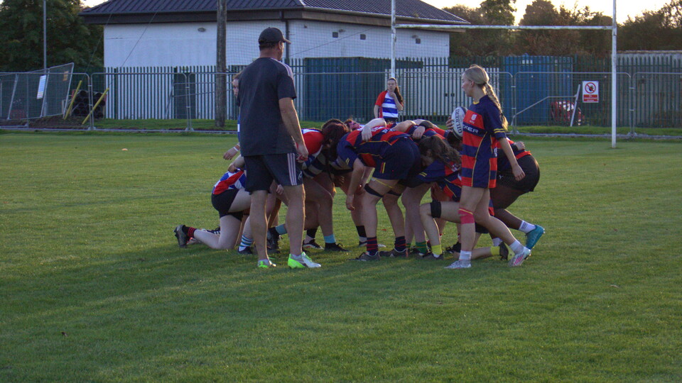 Rugby players in black and red jerseys huddle together on the grass field.