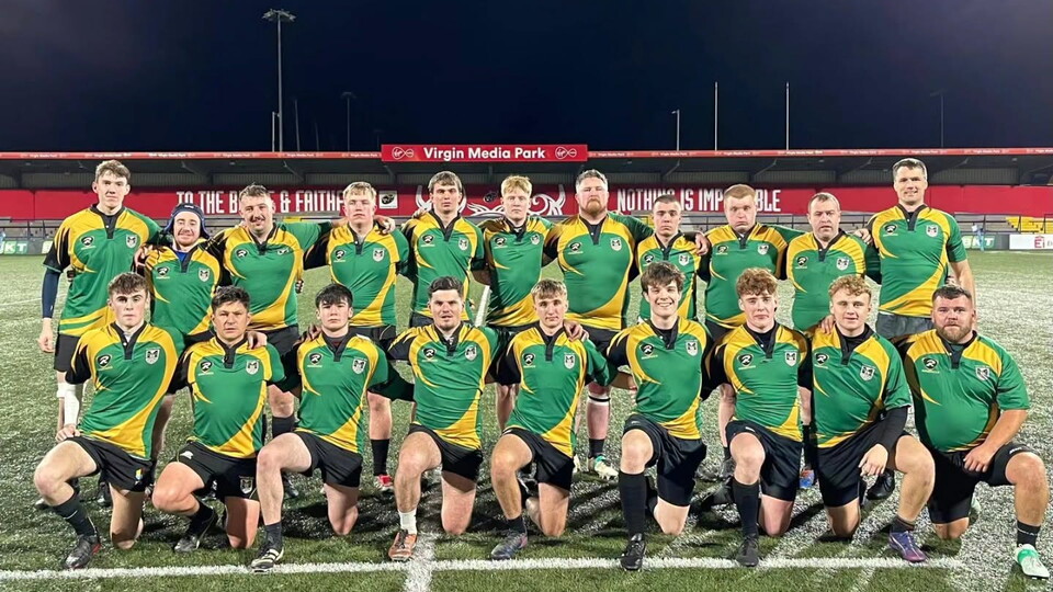 A rugby team in green and yellow kits pose for a photo on a pitch at night