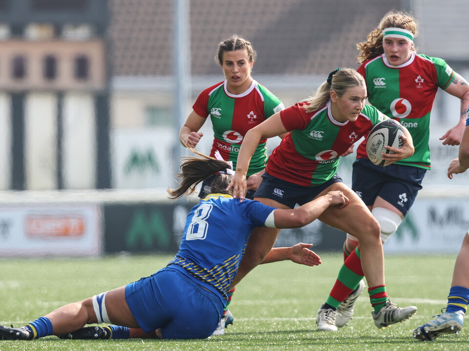 Players in red, green and blue jerseys play rugby on a field.
