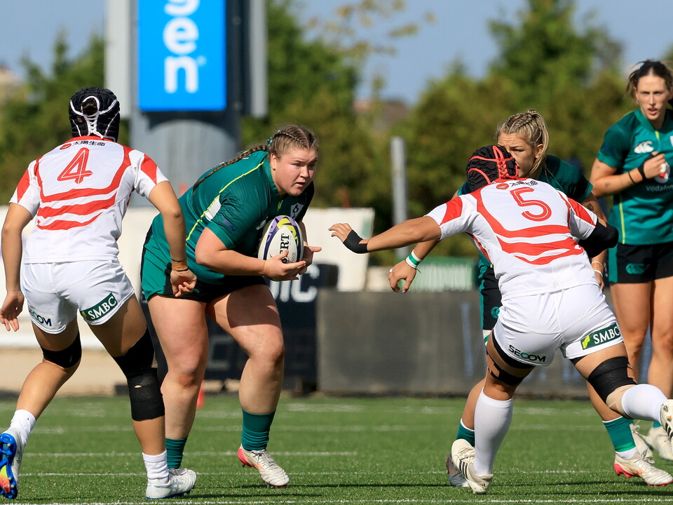 Women rugby players in green and white jerseys on a field, one player holds the ball.