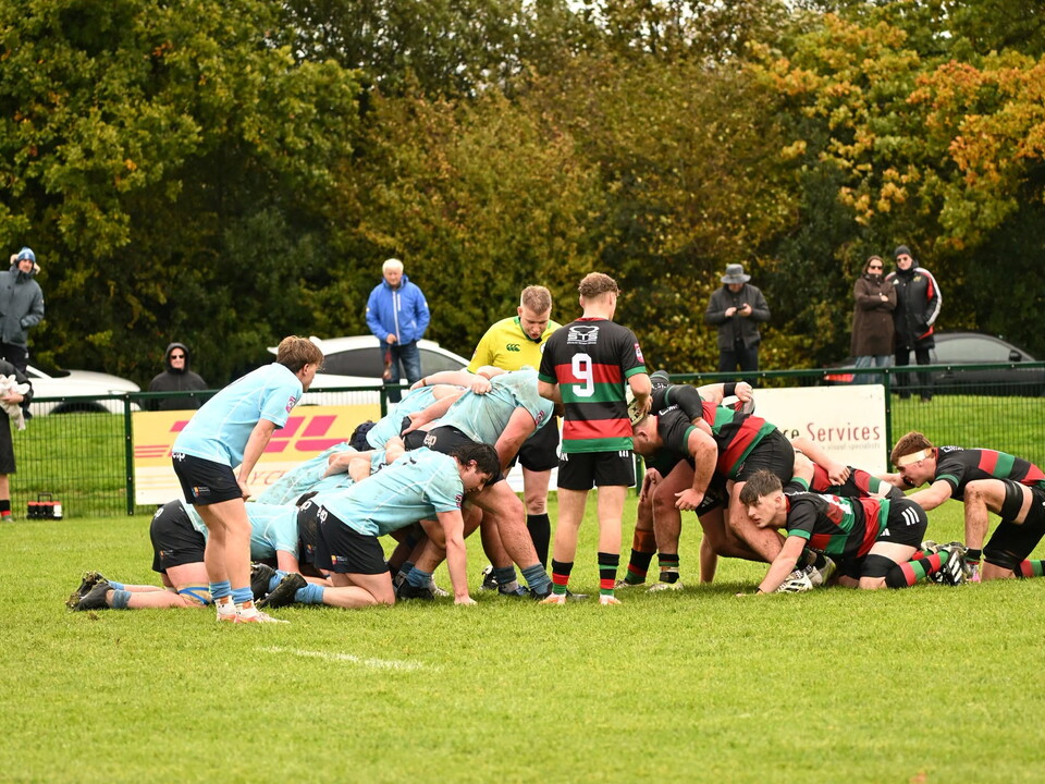 Players in maroon and black stripes scrum against players in blue jerseys.