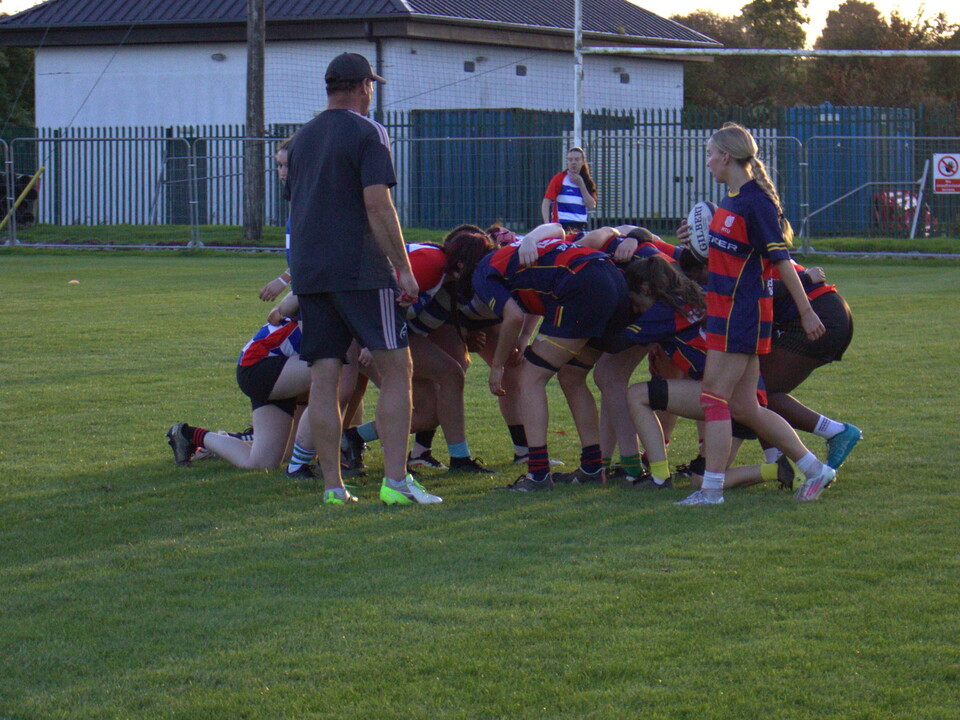 Rugby players in black and red jerseys huddle together on the grass field.