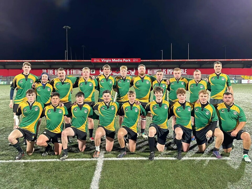 A rugby team in green and yellow kits pose for a photo on a pitch at night